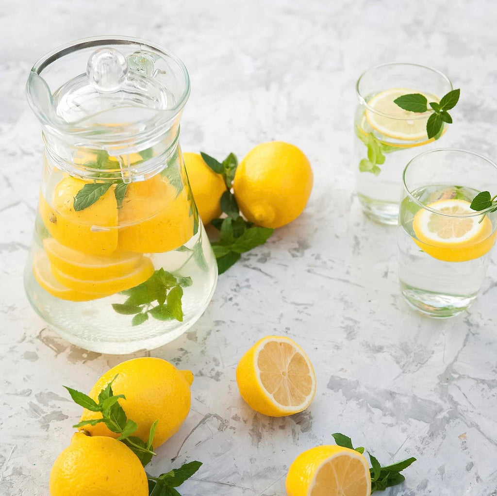 En tillbringare med citronvatten omgiven av gula citroner